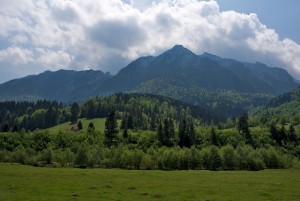 The ridge of the Piatra Craiului Mountains seen while driving back from Plaiul Foii into Zarnesti on a lovely summer day. Above them there are some white clouds blocking part of the sun.